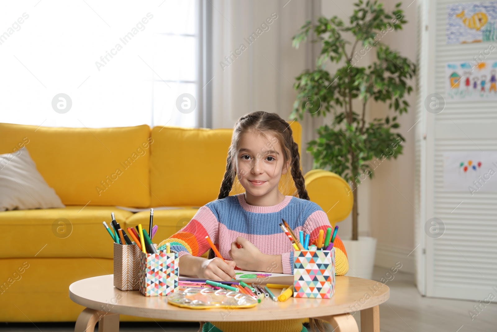 Photo of Little girl drawing picture at table with painting tools indoors