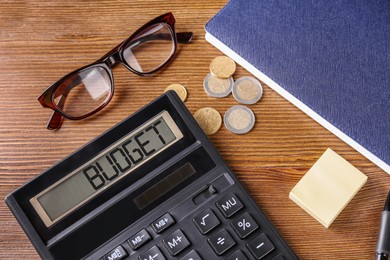 Image of Budget plan. Calculator, glasses, coins and notebook on wooden table, above view