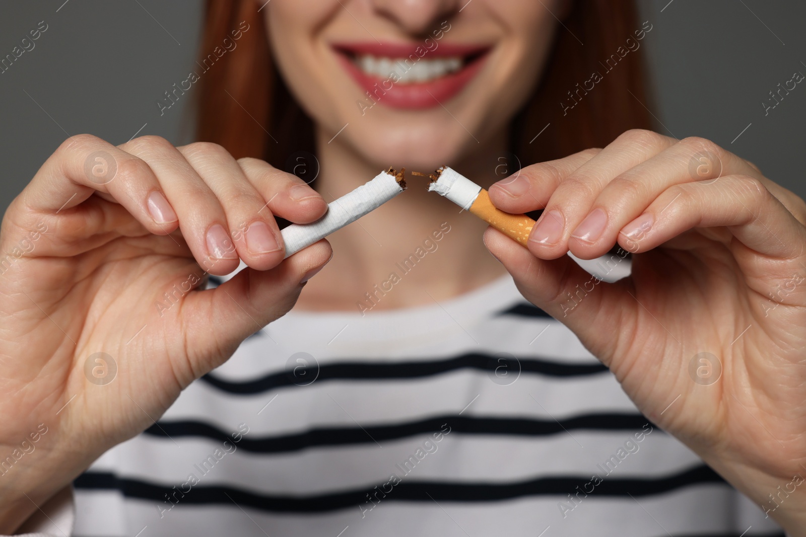 Photo of Stop smoking concept. Woman holding pieces of broken cigarette on gray background, closeup