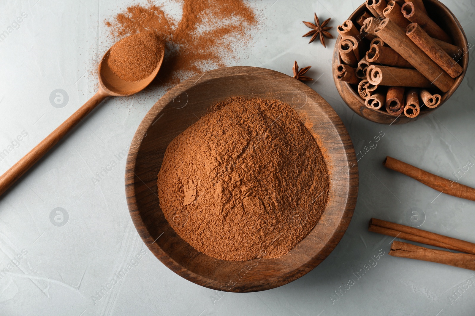 Photo of Bowls with aromatic cinnamon powder and sticks on grey background