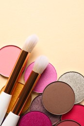 Different beautiful eye shadows and makeup brushes on beige background, flat lay. Space for text