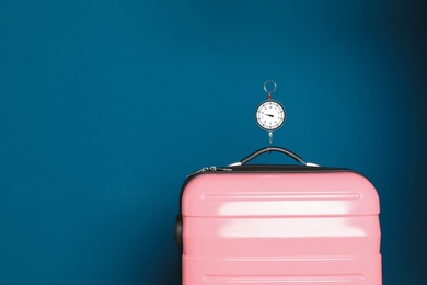 Modern suitcase and hanging scales against color background, space for text