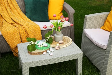 Easter decorations. Bouquet of tulips in vase, bunny figures and decorated eggs on table in backyard