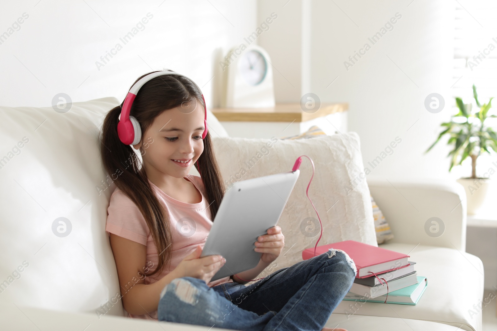 Photo of Cute little girl with headphones and tablet listening to audiobook at home