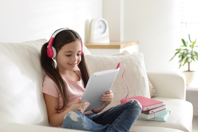 Cute little girl with headphones and tablet listening to audiobook at home