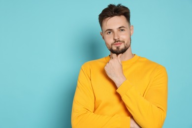 Handsome man in yellow sweatshirt on light blue background, space for text