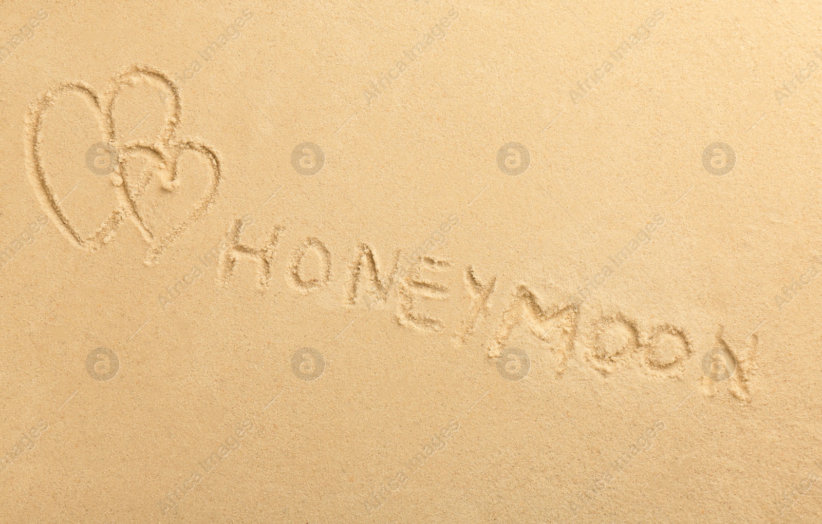 Photo of Word Honeymoon written on sand and hearts, top view