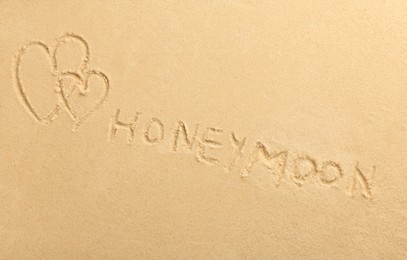 Photo of Word Honeymoon written on sand and hearts, top view