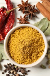 Photo of Curry powder in bowl and other spices on white wooden table, flat lay