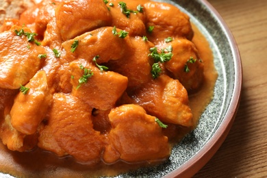 Photo of Plate of delicious butter chicken on wooden table, closeup. Traditional Murgh Makhani dish