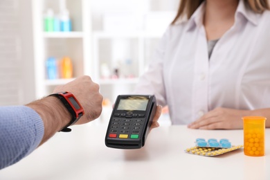 Photo of Man using terminal for contactless payment with smart watch in pharmacy, closeup. Space for text