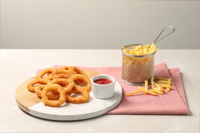 Tasty ketchup, fries and onion rings on light grey table, space for text