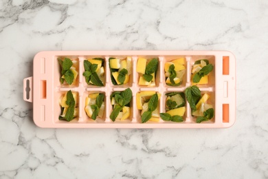 Photo of Ice cube tray with mint and lemon on marble background, top view