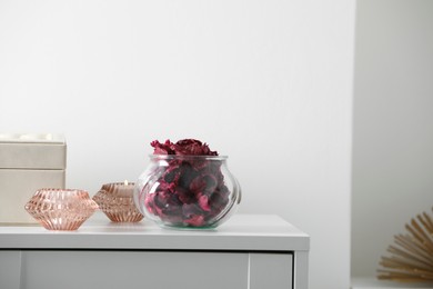 Photo of Glass jar with aromatic potpourri and burning candles on white chest of drawers in room, space for text
