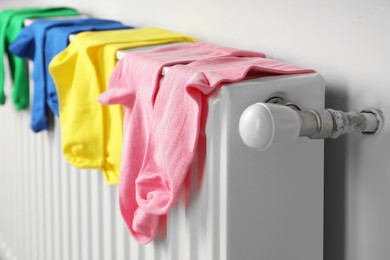 Photo of Different colorful socks hanging on white radiator indoors, closeup