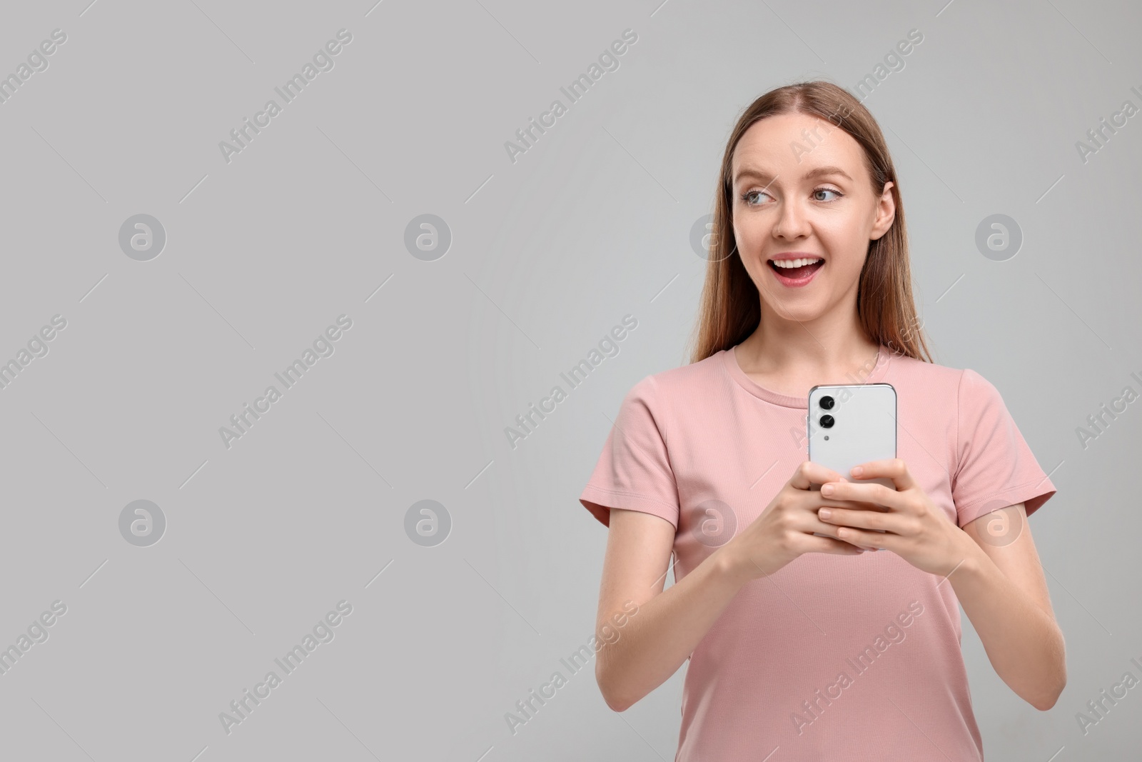 Photo of Happy woman sending message via smartphone on grey background, space for text