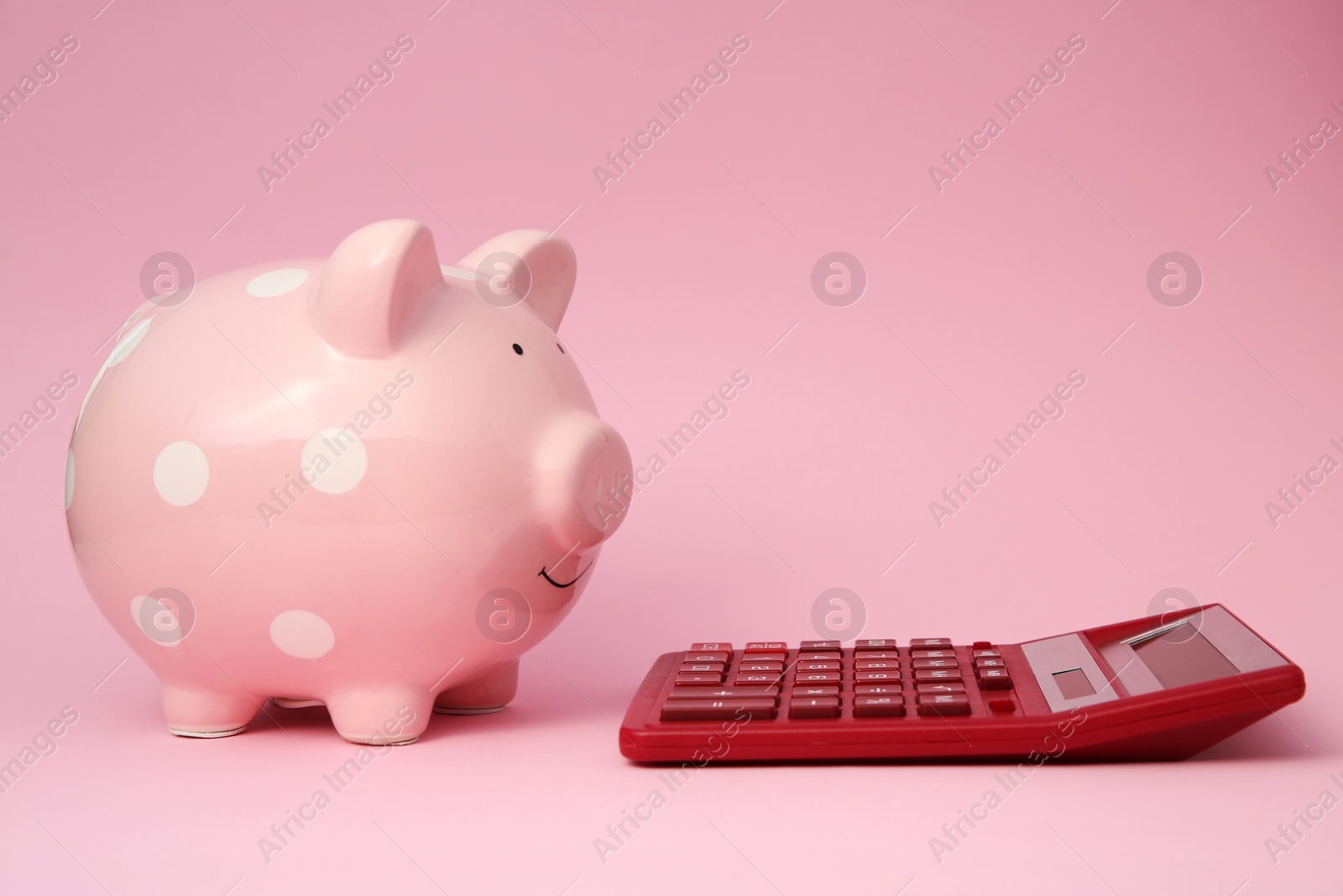 Photo of Piggy bank and calculator on pink background