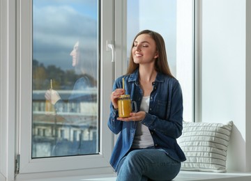 Beautiful young woman with delicious smoothie near window. Space for text