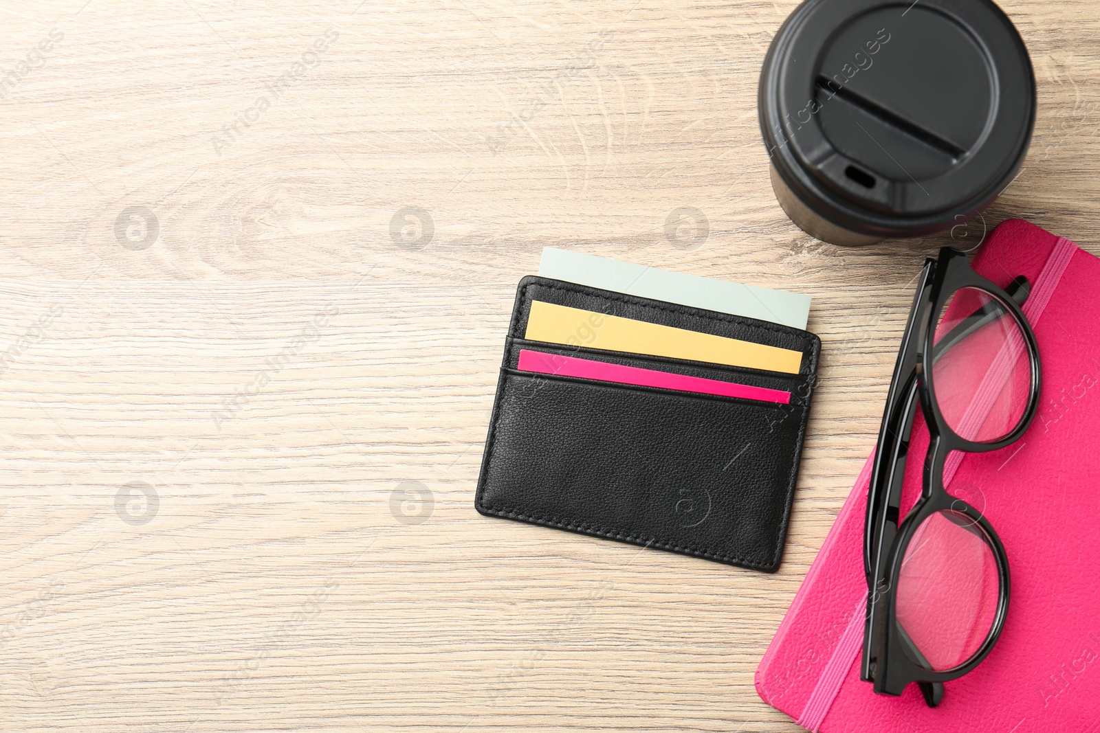 Photo of Leather business card holder with colorful cards, stationery, glasses and coffee on wooden table, flat lay. Space for text