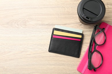 Photo of Leather business card holder with colorful cards, stationery, glasses and coffee on wooden table, flat lay. Space for text