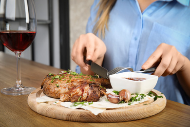 Photo of Woman eating delicious grilled pork chop at wooden table indoors, closeup