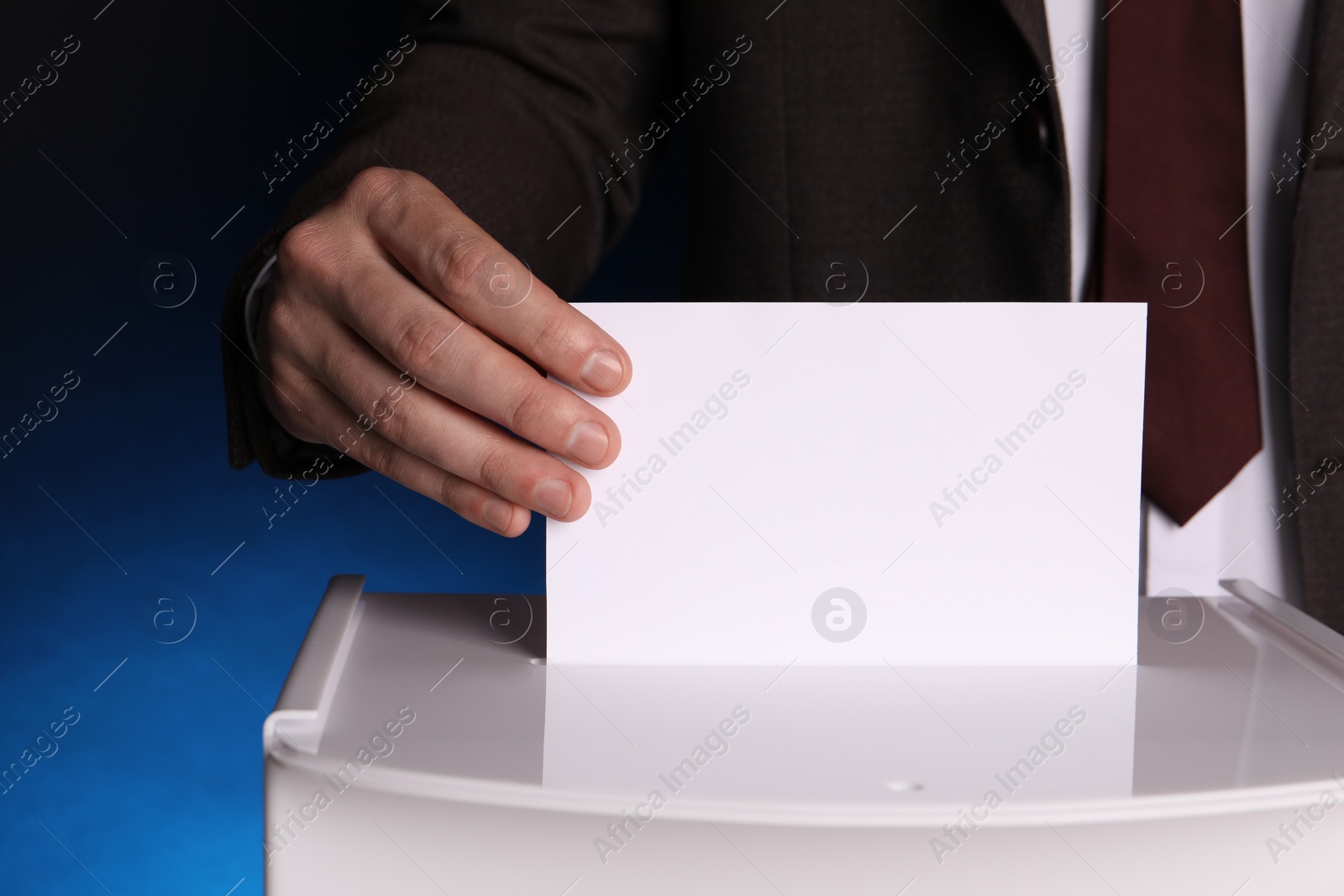 Photo of Man putting his vote into ballot box on dark blue background, closeup