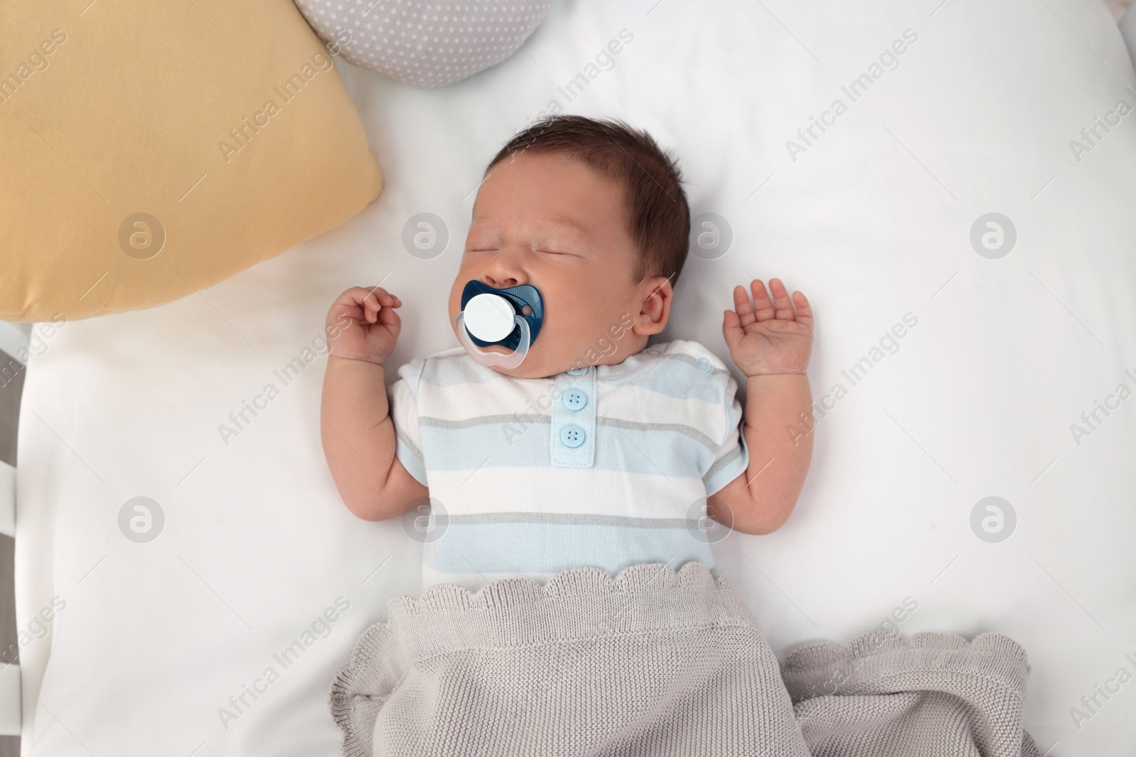 Photo of Cute newborn baby with pacifier sleeping under blanket in crib, top view. Bedtime