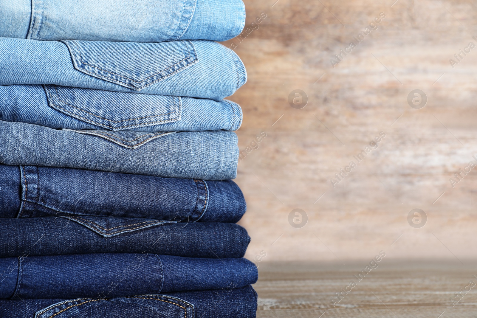 Photo of Stack of different jeans on wooden table. Space for text