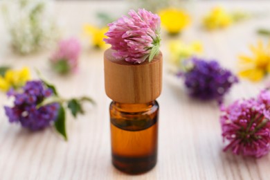 Bottle of essential oil and flowers on white wooden table, closeup