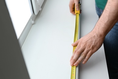 Man measuring white windowsill indoors, closeup. Construction tool