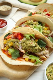 Delicious tacos with guacamole, meat and vegetables on white wooden table, closeup