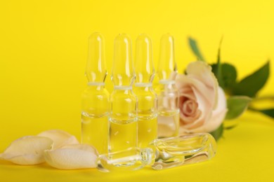 Pharmaceutical ampoules with medication and flower on yellow background, closeup