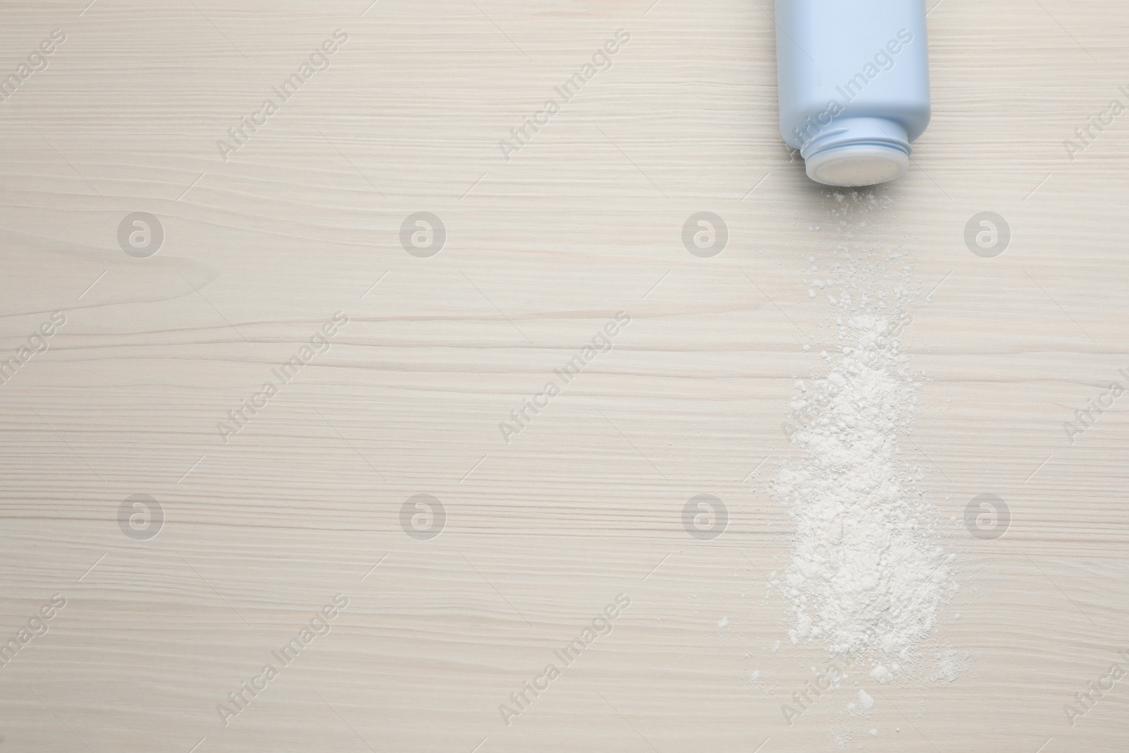 Photo of Bottle and scattered dusting powder on white wooden background, top view with space for text. Baby cosmetic product