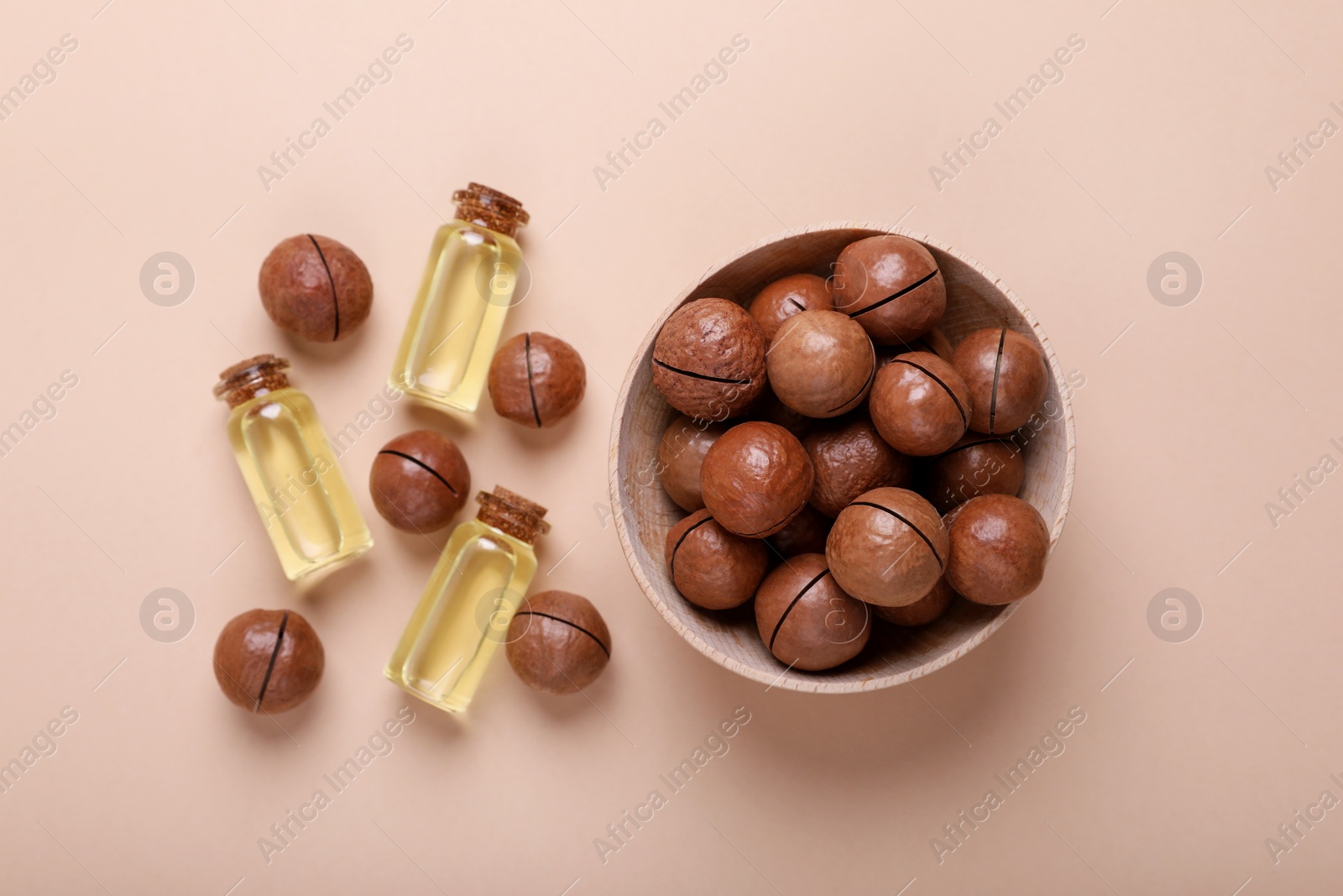 Photo of Delicious organic Macadamia nuts and cosmetic oil on beige background, flat lay