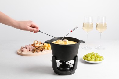 Woman dipping ham into fondue pot with tasty melted cheese at white table, closeup
