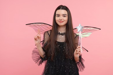 Photo of Beautiful girl in fairy costume with wings and magic wand on pink background