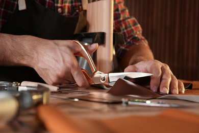 Photo of Man cutting leather with scissors at table, closeup