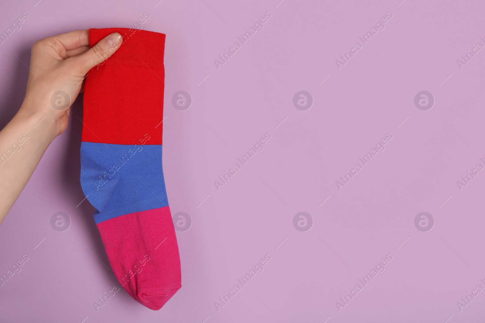 Photo of Woman holding striped sock on light violet background, closeup. Space for text