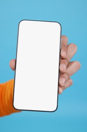 Man holding smartphone with blank screen on light blue background, closeup