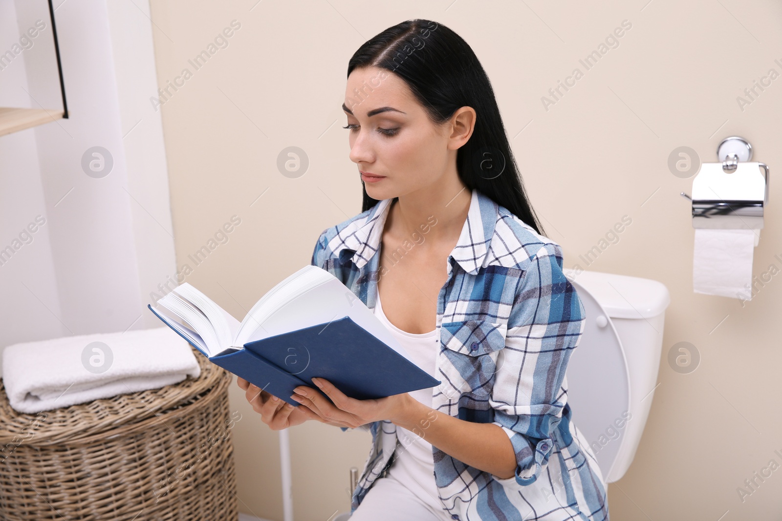 Photo of Woman with book sitting on toilet bowl in bathroom