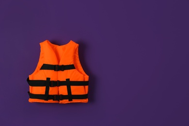 Photo of Orange life jacket on violet background. Space for text