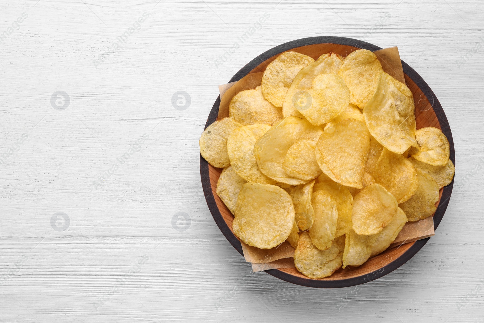 Photo of Delicious crispy potato chips in bowl on table, top view with space for text