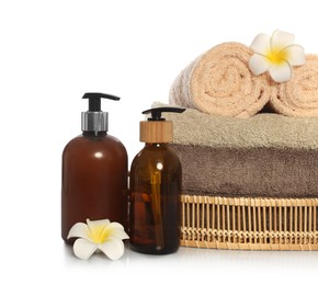 Photo of Soft towels in wicker basket, bottles of cosmetic products and plumeria flowers on white background