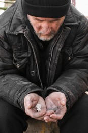 Photo of Poor homeless senior man holding coins outdoors