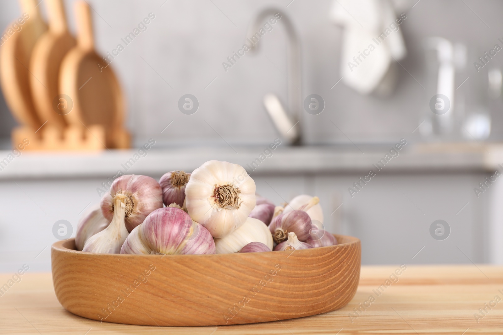 Photo of Bowl of fresh raw garlic on wooden table in kitchen