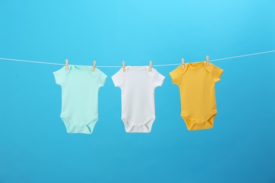 Photo of Colorful baby onesies hanging on clothes line against blue background. Laundry day