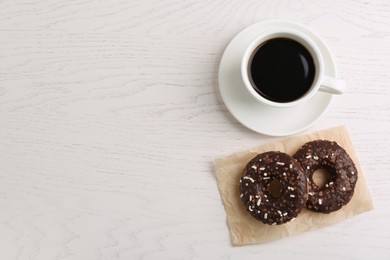 Photo of Two delicious fresh donuts with sprinkles and cup of coffee on white wooden table, flat lay. Space for text