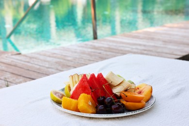 Photo of Plate with fresh fruits on sun lounger near outdoor swimming pool. Luxury resort