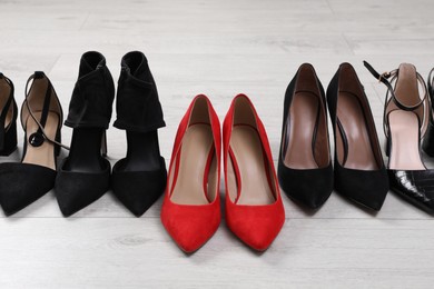 Red shoes among black ones on light wooden floor. Diversity concept
