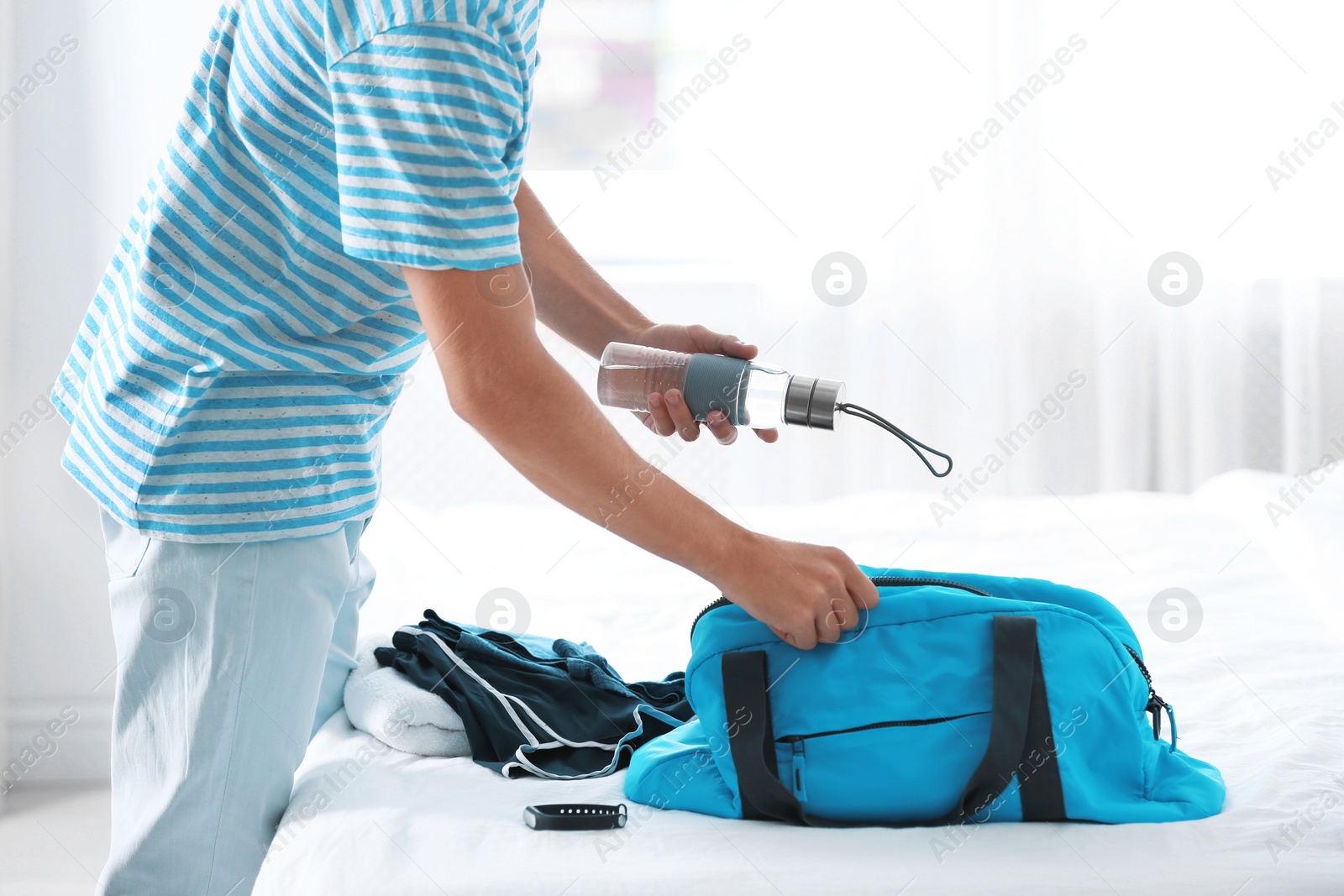 Photo of Young man packing sports stuff for training into bag in bedroom